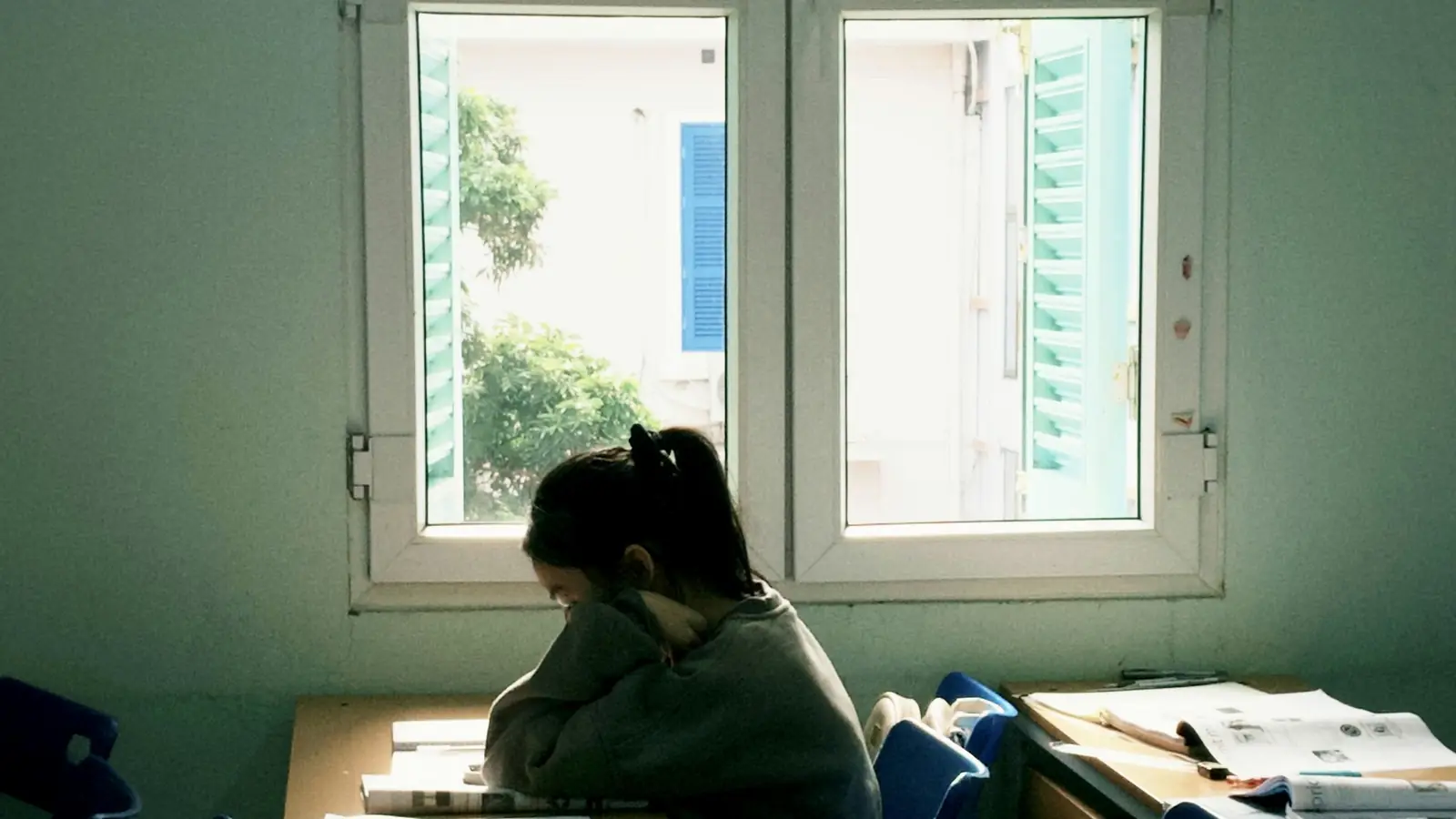 A person slumped with their head down on a desk by a window