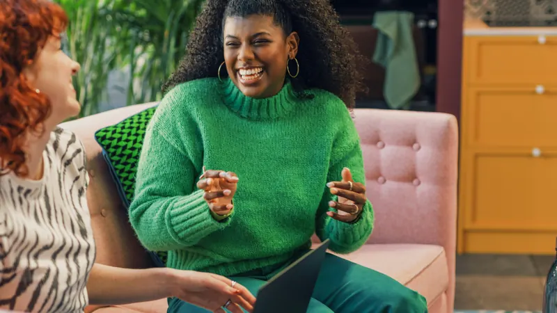 A woman in a green sweater laughing with a colleague